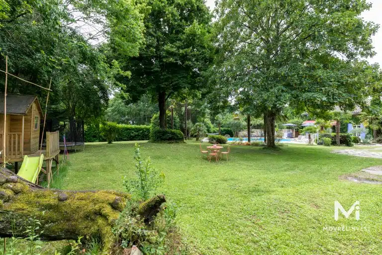 Jardin verdoyant avec piscine et maisonnette en bois.