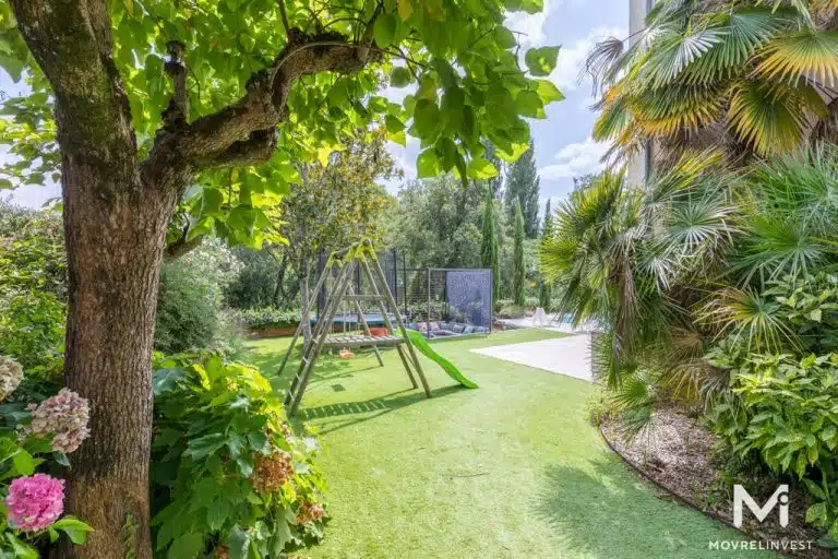 Jardin verdoyant avec aire de jeux et palmiers.