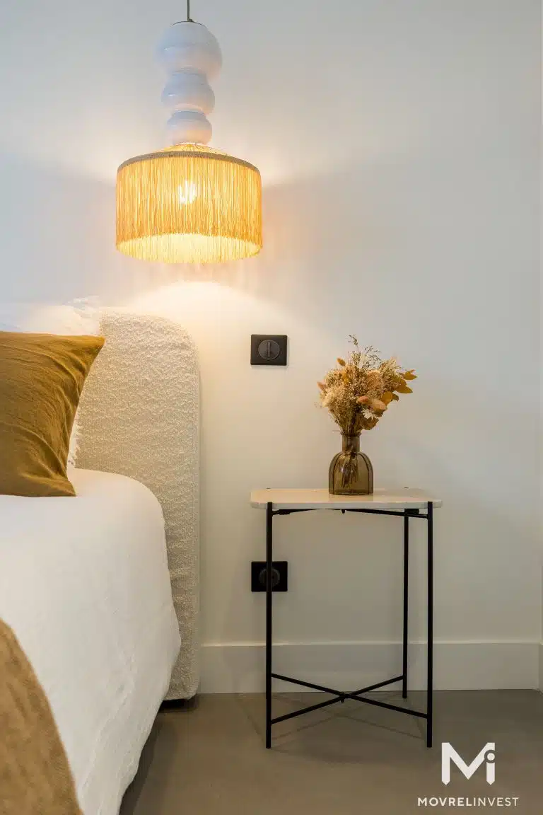 Chambre moderne avec suspension lumineuse et table de chevet.
