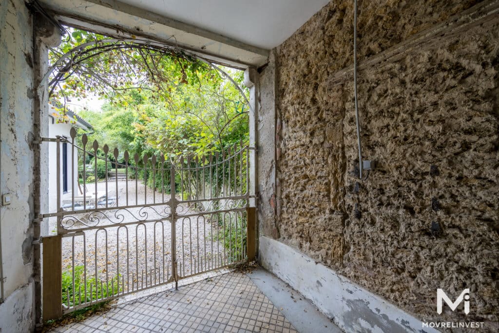 Portail ouvert sur un jardin, murs en pierre décrépis