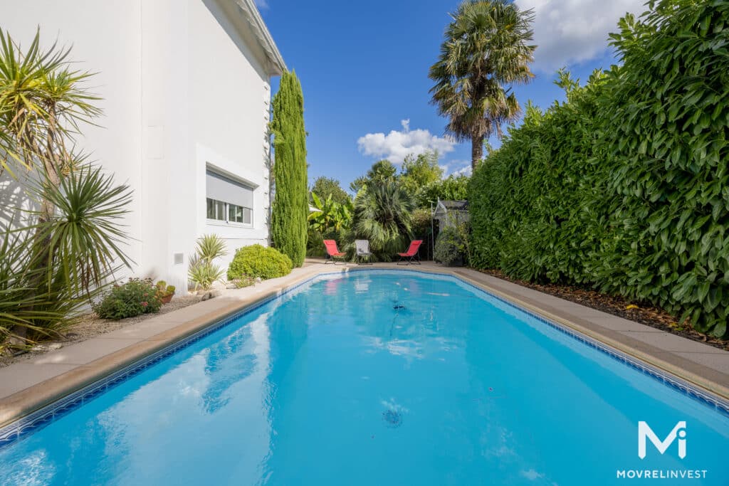 Piscine extérieure ensoleillée avec transats et jardin luxuriant