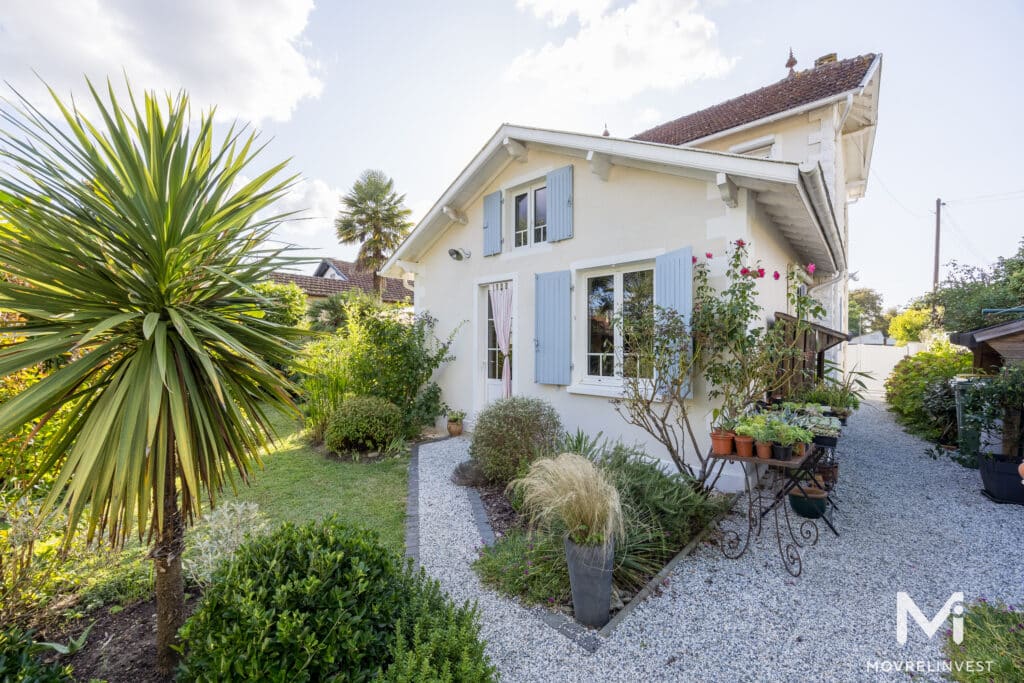 Maison blanche avec volets bleus et jardin verdoyant