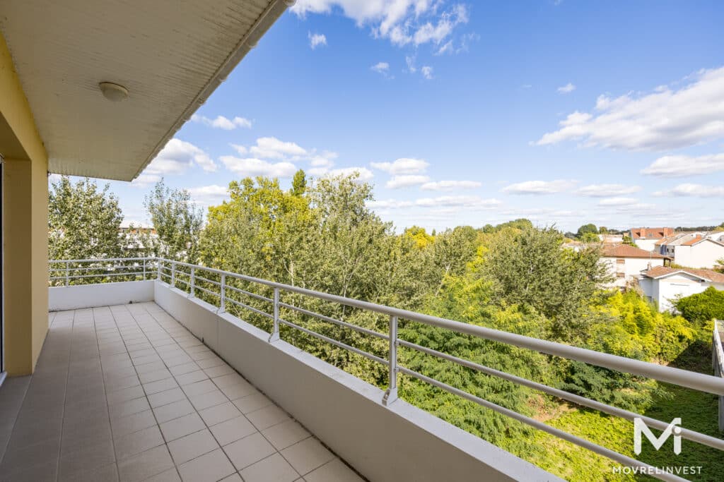 Grand balcon avec vue sur des arbres et ciel nuageux