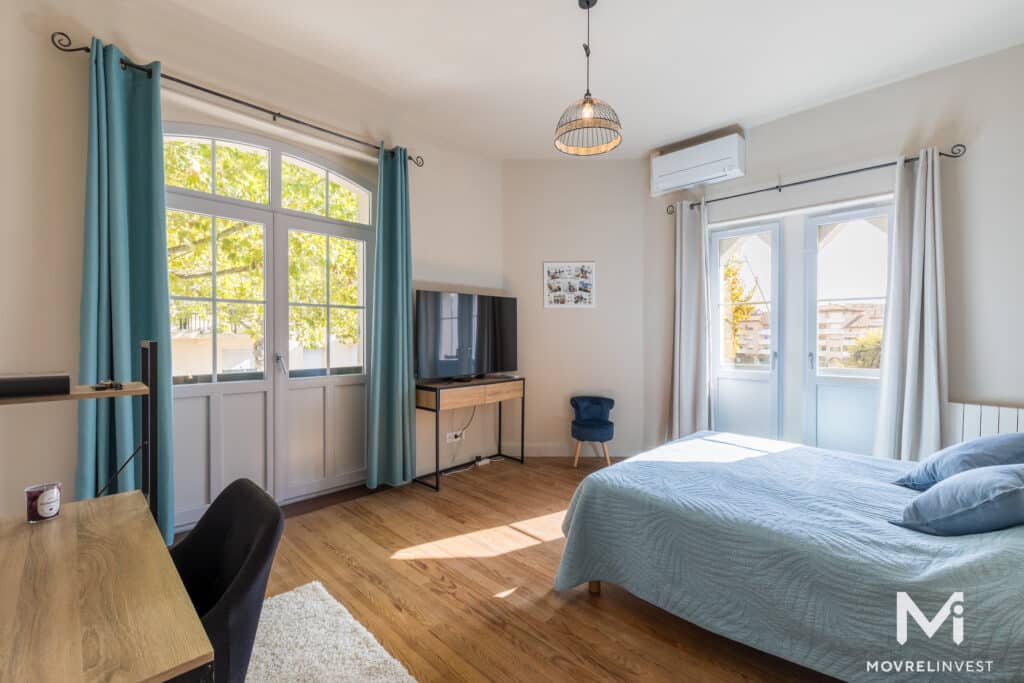 Chambre lumineuse avec lit, bureau et fenêtres ouvertes