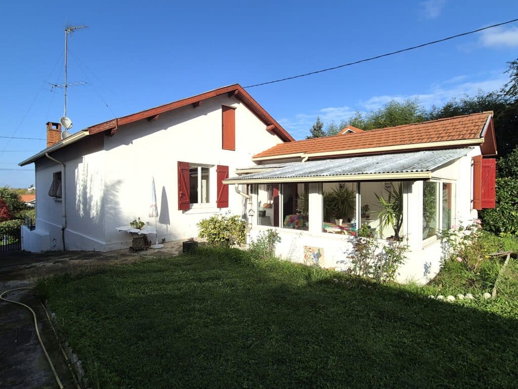 Maison blanche avec véranda et volets rouges, jardin vert